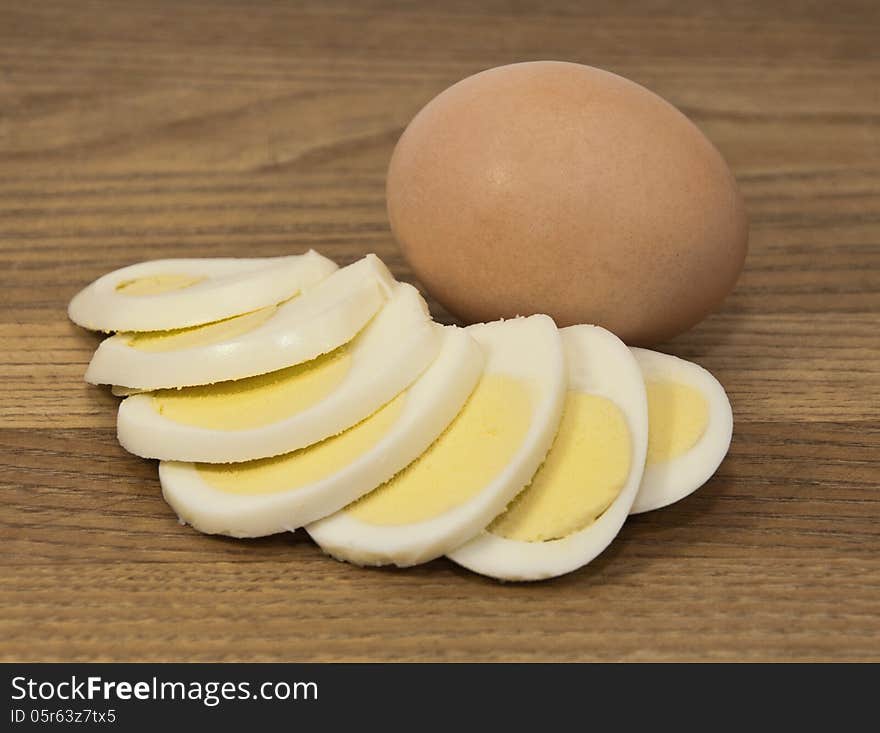 Brown egg and boiled egg slices against a brown wood grained background. Brown egg and boiled egg slices against a brown wood grained background