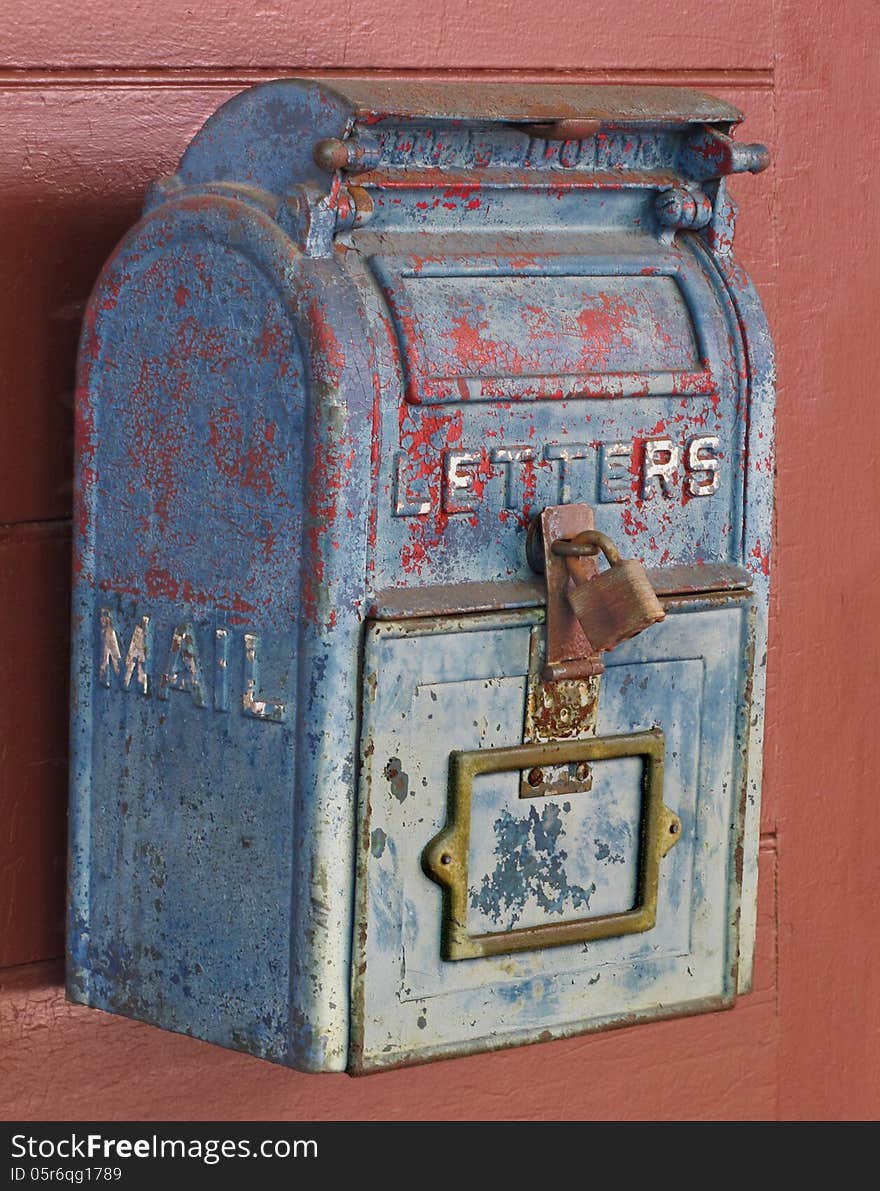 Close-up of an old, weathered, and worn blue metal mailbox with peeling paint, on a red wooden door. Close-up of an old, weathered, and worn blue metal mailbox with peeling paint, on a red wooden door.