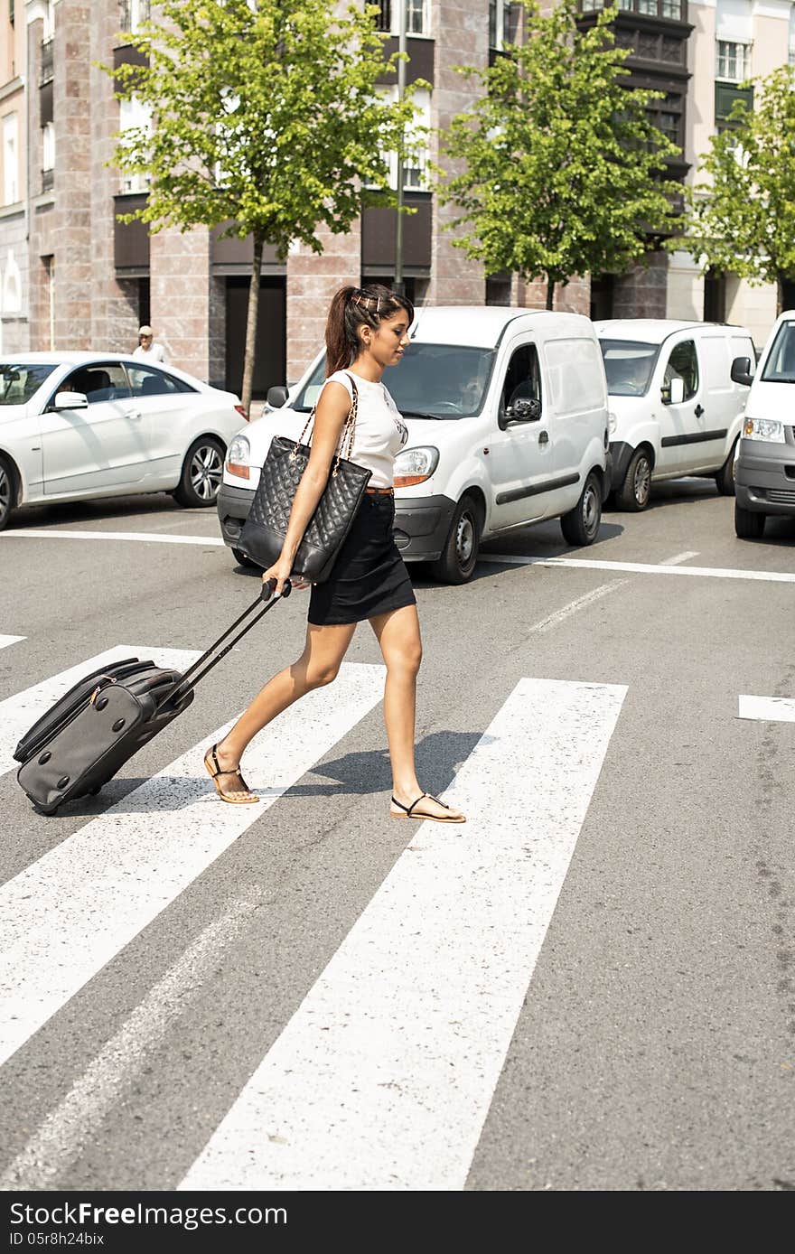 Business woman crossing the street with luggage.