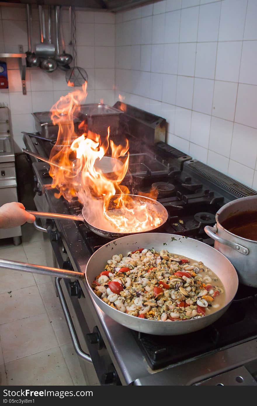 Cooking seafood with tomatoes for pizza in Italian pizzeria and fire view in a pan while frying onion. Cooking seafood with tomatoes for pizza in Italian pizzeria and fire view in a pan while frying onion.