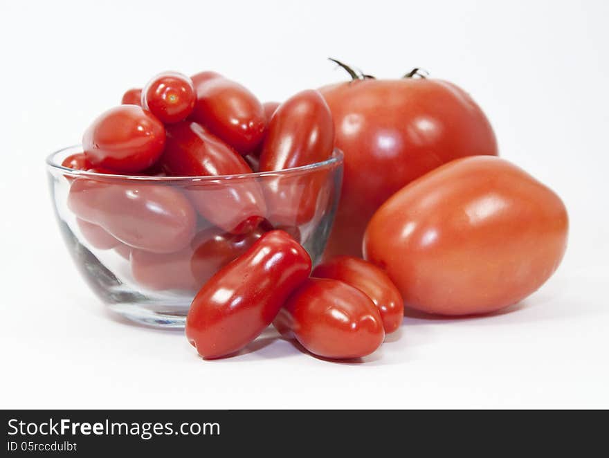 Three types and sizes of red tomatoes and a clear glass bowl against a white background. Three types and sizes of red tomatoes and a clear glass bowl against a white background