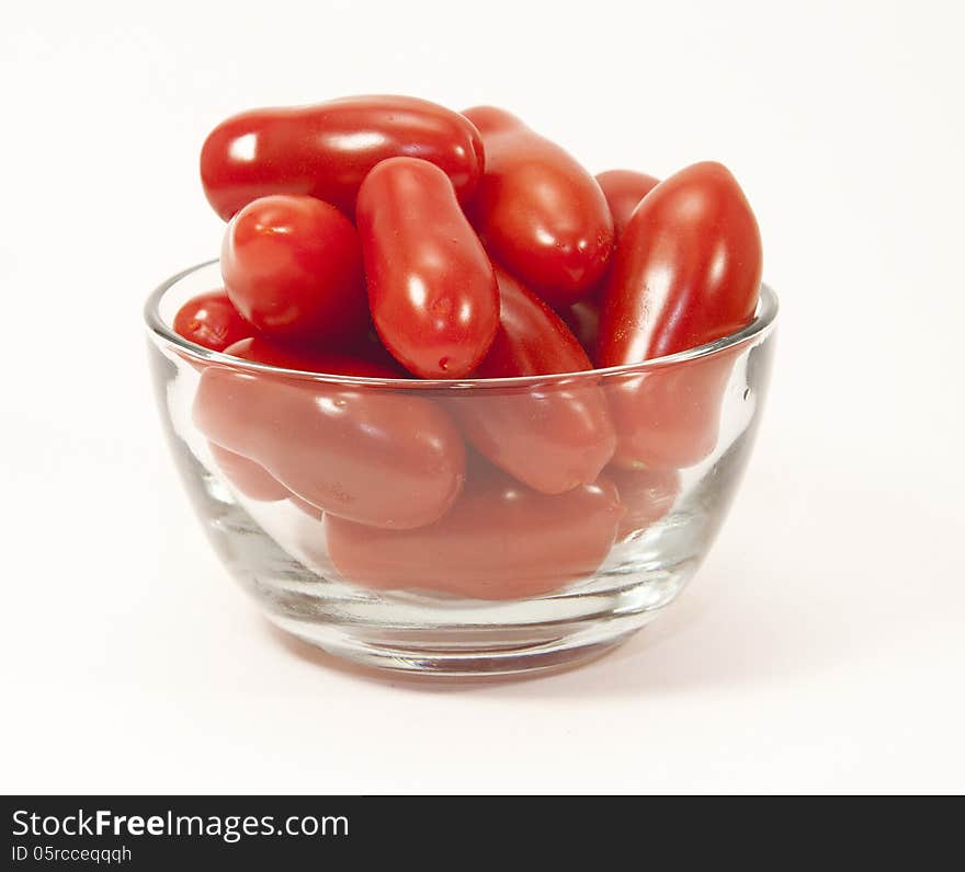 Mini red tomatoes in a clear glass bowl against a white background. Mini red tomatoes in a clear glass bowl against a white background