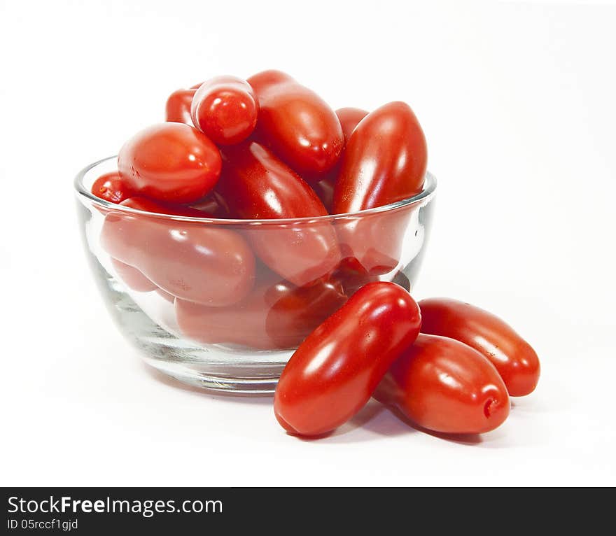 Mini red tomatoes in and next to a glass bowl against a white background. Mini red tomatoes in and next to a glass bowl against a white background