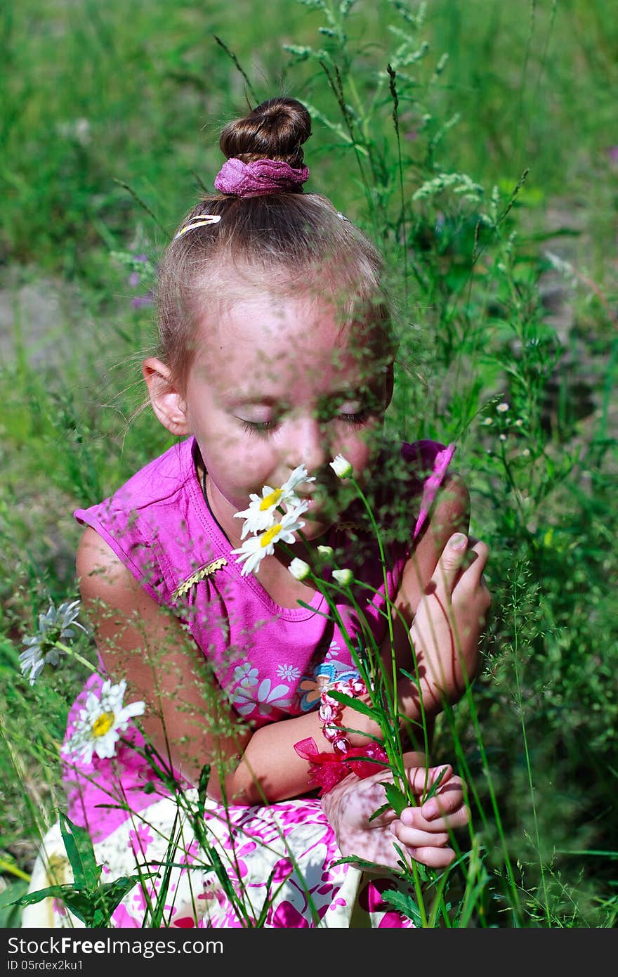 Happy little girl in grass smelling daisies