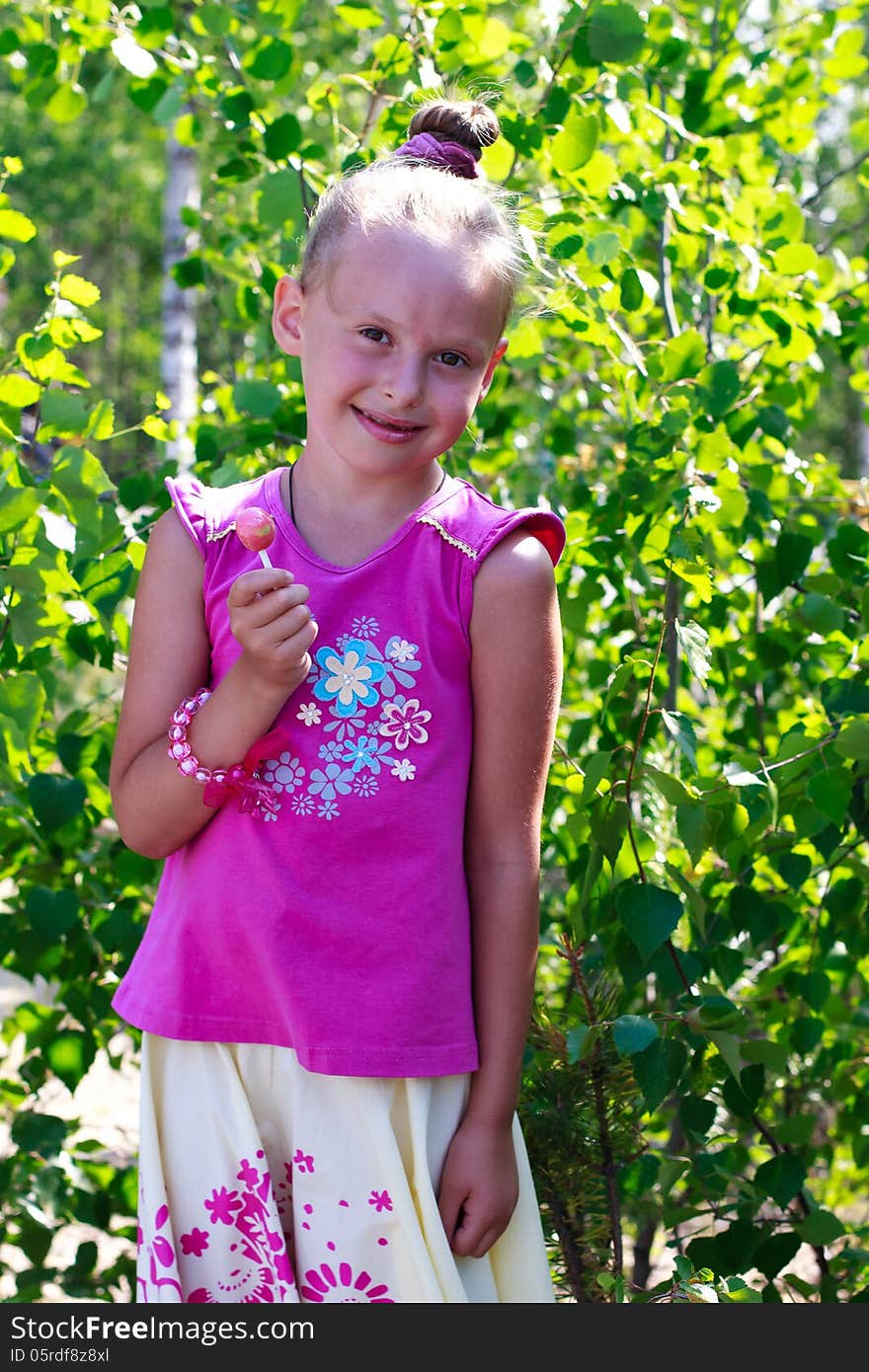 A portrait of a cute little girl holding candy in a tree shade. A portrait of a cute little girl holding candy in a tree shade