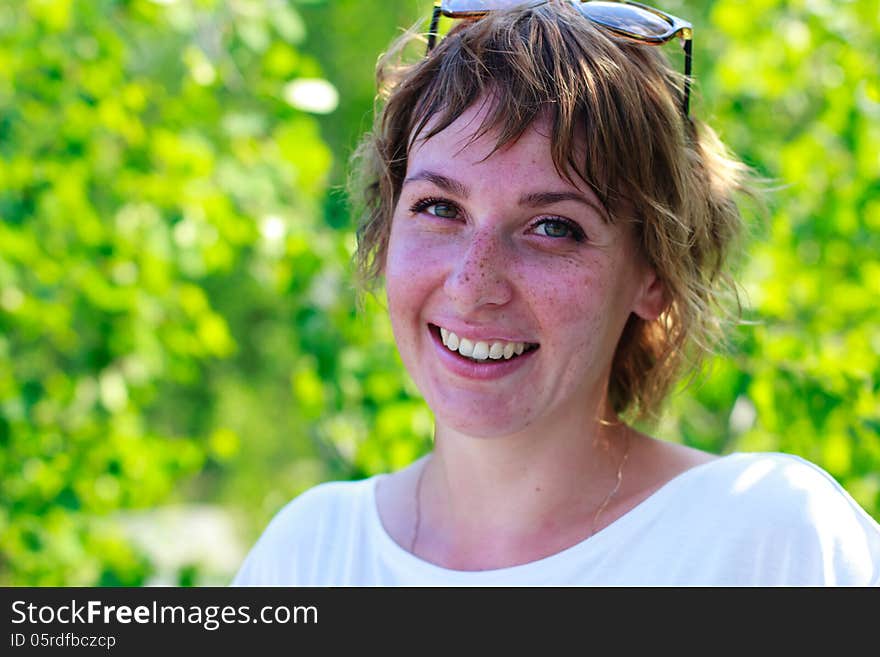 Young girl with freckles smiles on the background of green leaves. Young girl with freckles smiles on the background of green leaves