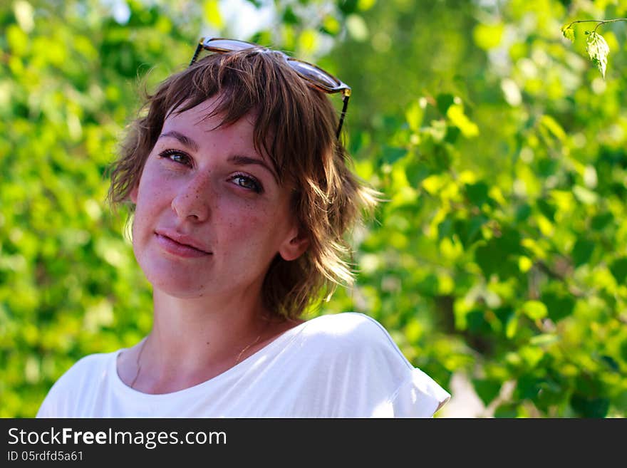 Young girl with freckles on the background of green leaves. Young girl with freckles on the background of green leaves