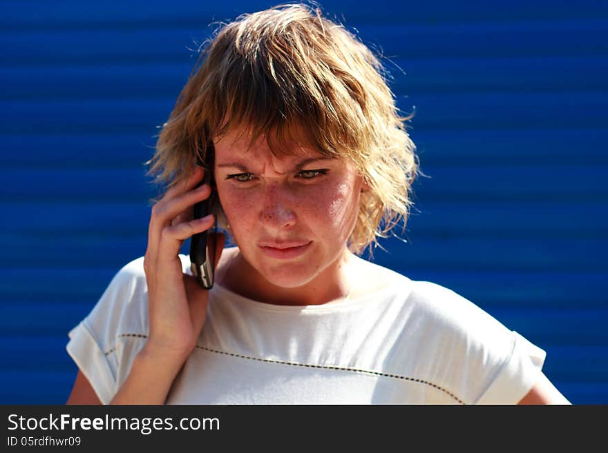 The girl got angry talking on the phone over blue striped background. The girl got angry talking on the phone over blue striped background