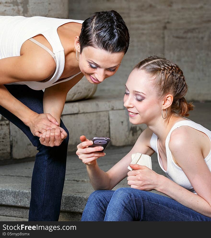 Family, mother and daughter are sitting on the steps of the library and looking at mobile phone