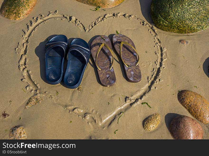 A pair of male and a pair of female footwear standing in heart shape on the beach. A pair of male and a pair of female footwear standing in heart shape on the beach