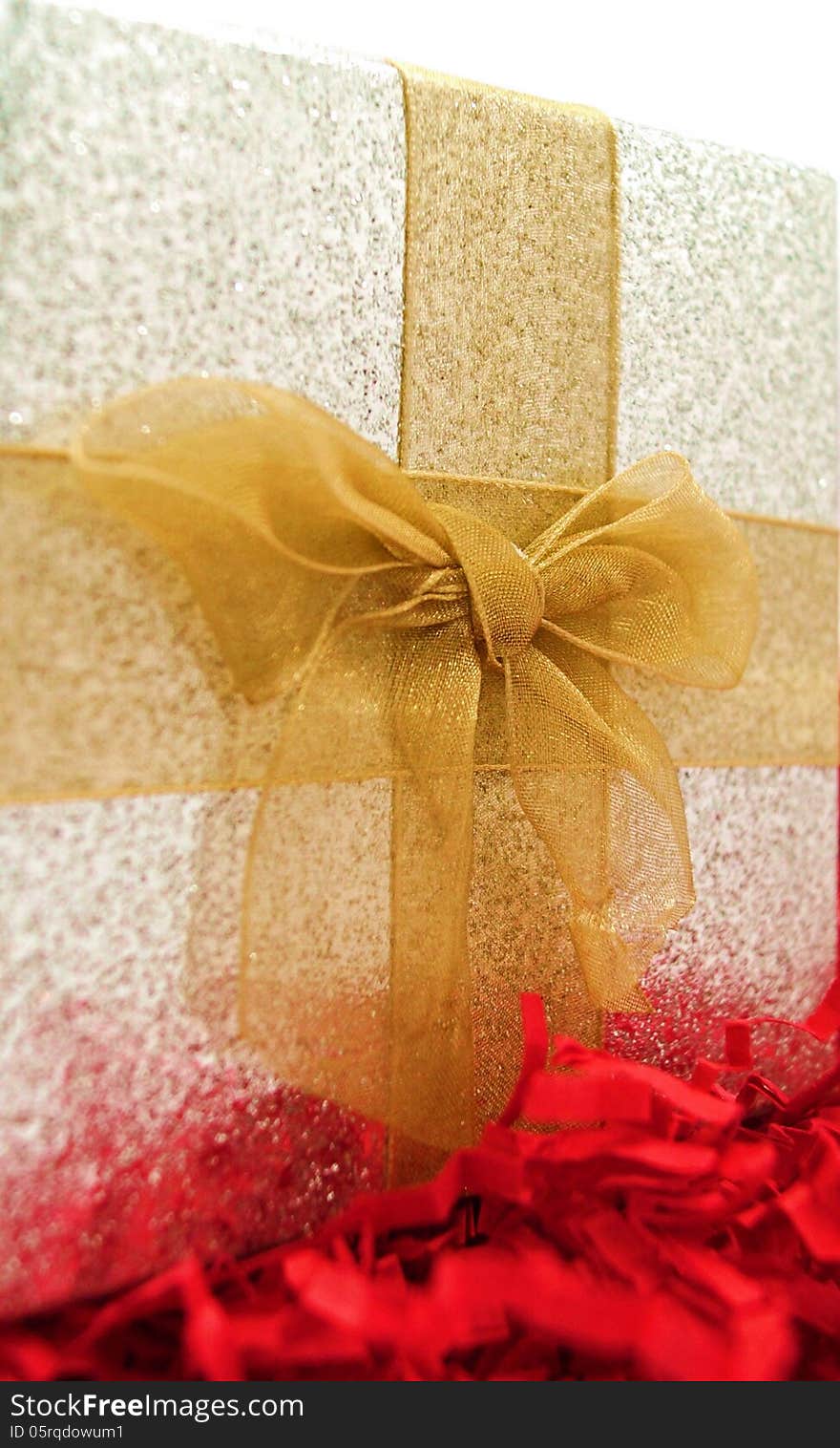 A sparkly silver gift box with gold ribbon rests on red fringe. A sparkly silver gift box with gold ribbon rests on red fringe.