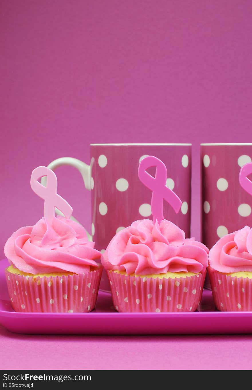 Pink cupcakes with Pink Ribbon symbol for International Breast Cancer Awareness charity month of October. with pink polka dot coffee mugs - vertical with copy space. Pink cupcakes with Pink Ribbon symbol for International Breast Cancer Awareness charity month of October. with pink polka dot coffee mugs - vertical with copy space.