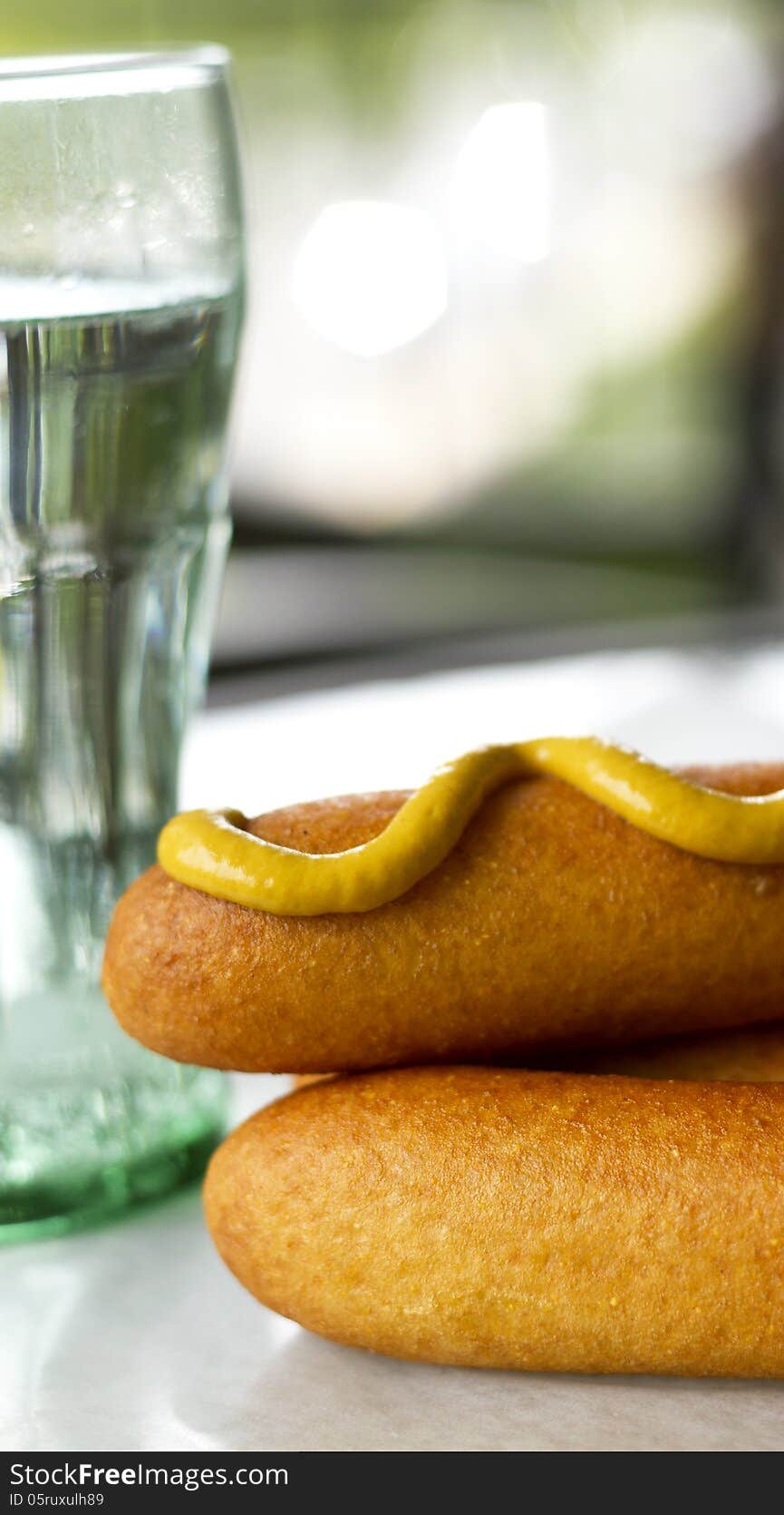 Close-up of corn dogs with mustard on with a drink in the background