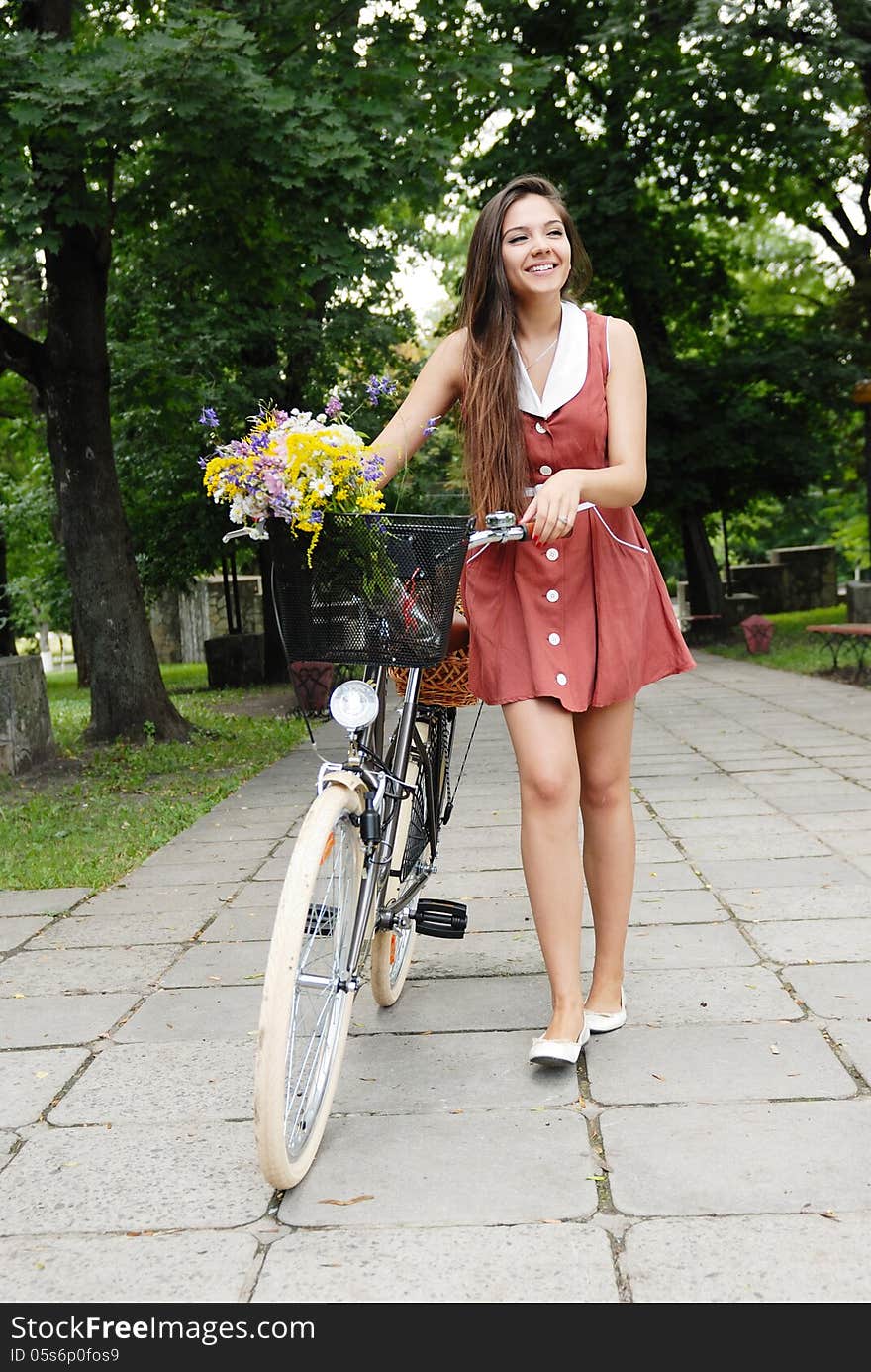 Fashion portrait of young pretty woman with bicycle and flowers