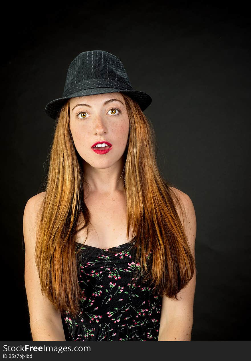 Very cute girl with red hair freckles and beautiful hazel eyes wearing a pinstriped fedora against a dark background. Very cute girl with red hair freckles and beautiful hazel eyes wearing a pinstriped fedora against a dark background