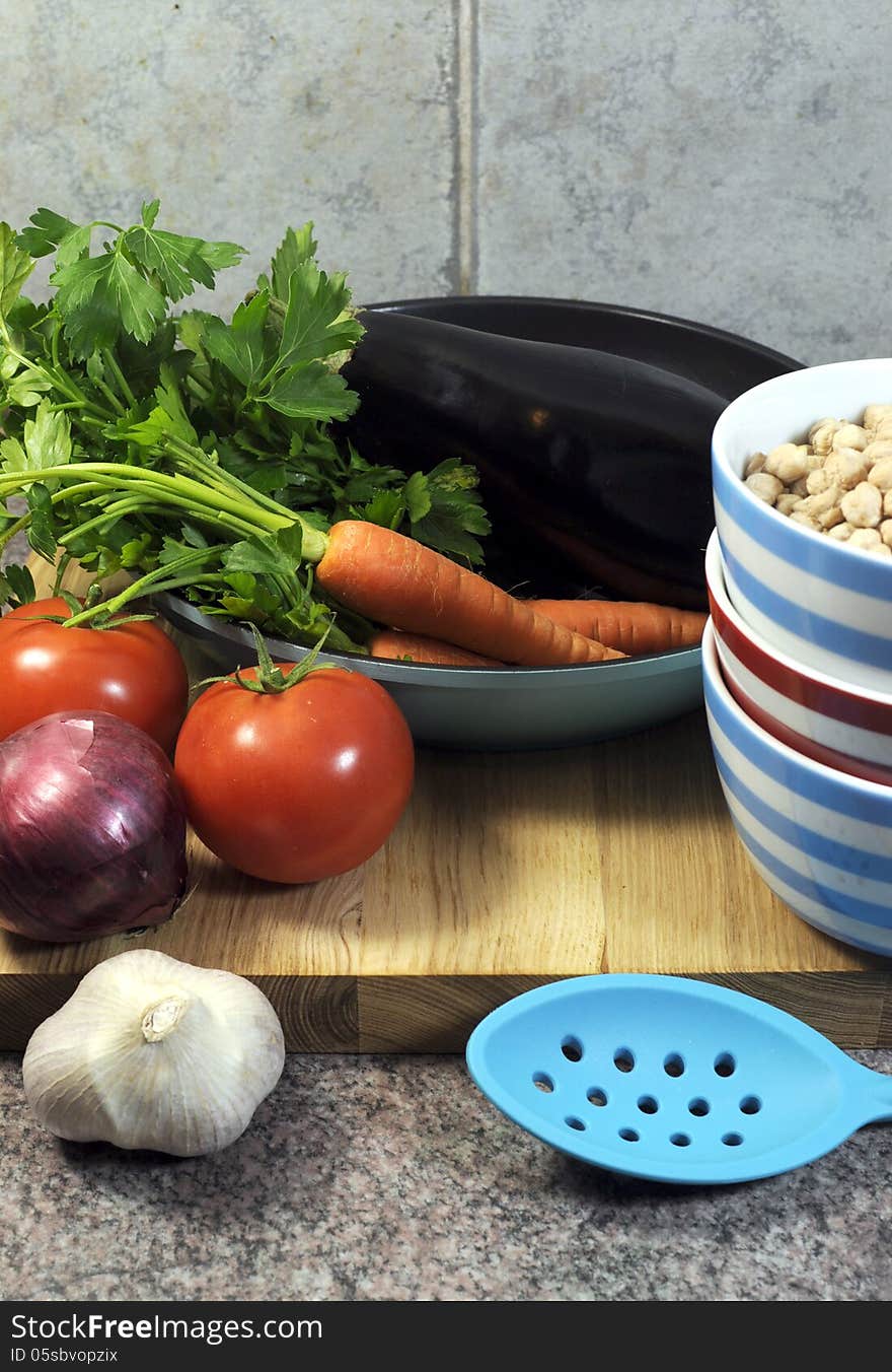 Vegetarian cooking concept with eggplant, carrots, tomatoes, and red onion with dried chick peas and blue, red and white cooking utensils for healthy diet concept or World Vegetarian Day on October 1. Vertical. Vegetarian cooking concept with eggplant, carrots, tomatoes, and red onion with dried chick peas and blue, red and white cooking utensils for healthy diet concept or World Vegetarian Day on October 1. Vertical.