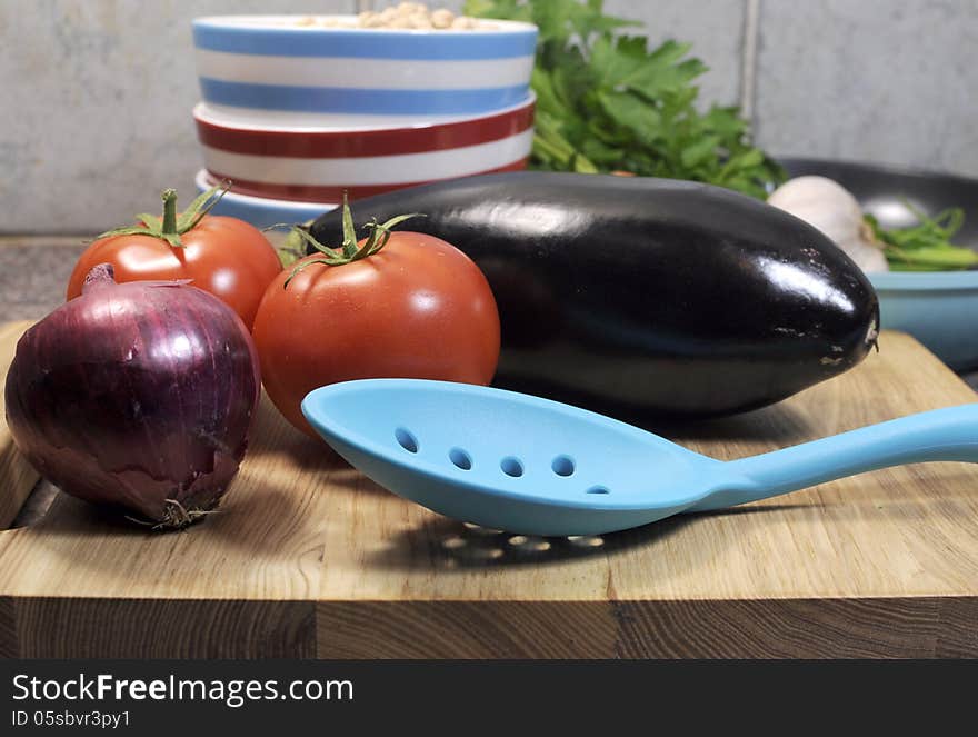 Vegetarian cooking concept with eggplant, carrots, tomatoes, and red onion with dried chick peas and blue, red and white cooking utensils for healthy diet concept or World Vegetarian Day on October 1. Close up. Vegetarian cooking concept with eggplant, carrots, tomatoes, and red onion with dried chick peas and blue, red and white cooking utensils for healthy diet concept or World Vegetarian Day on October 1. Close up.