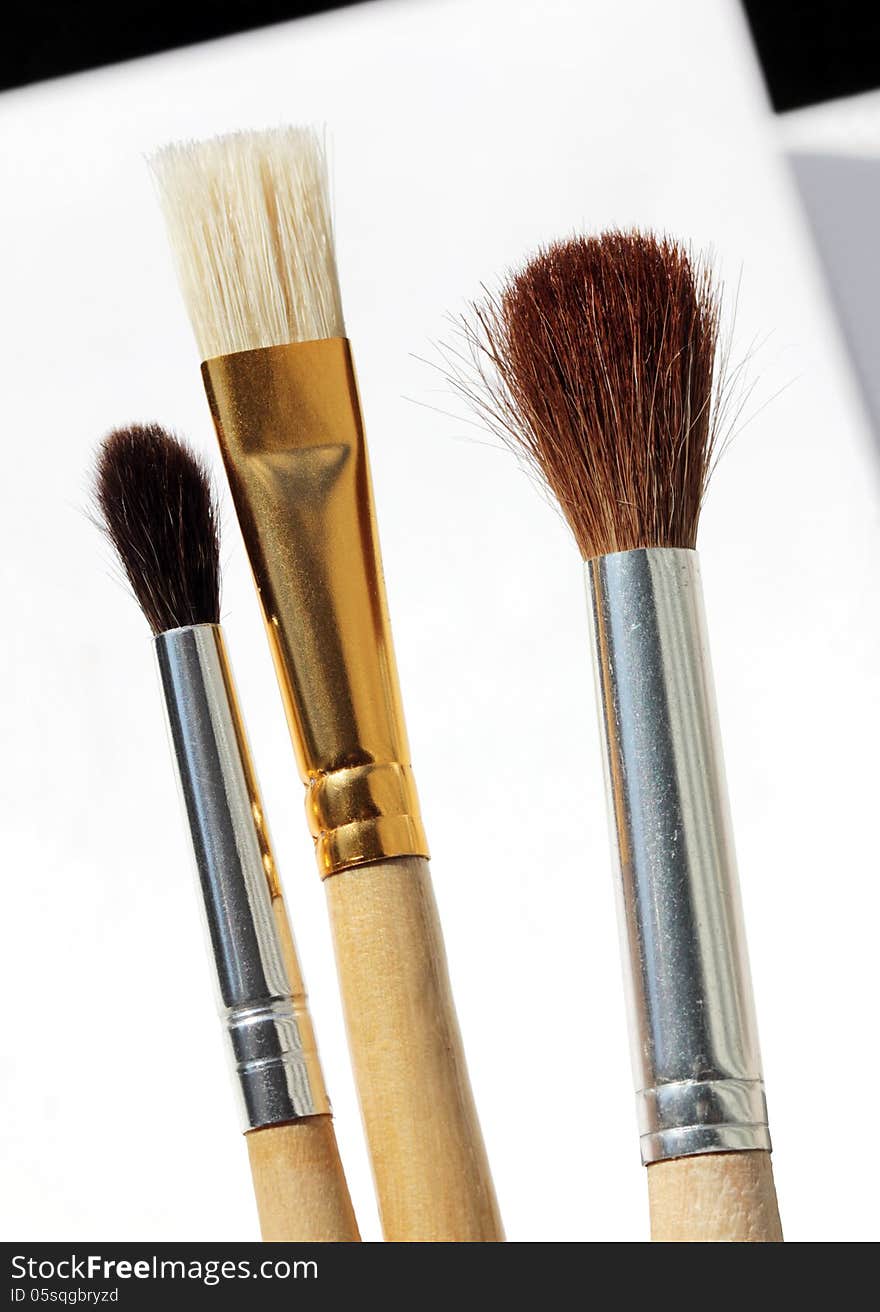 Close up view of three paint brushes against white paper sheets. Shallow depth, selective focus. Close up view of three paint brushes against white paper sheets. Shallow depth, selective focus.