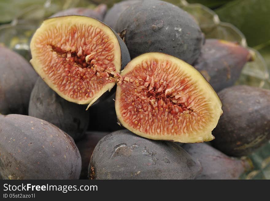 A pair of cut plump ripe mission figs on top of a harvest of more figs with a glass dish visible. A pair of cut plump ripe mission figs on top of a harvest of more figs with a glass dish visible