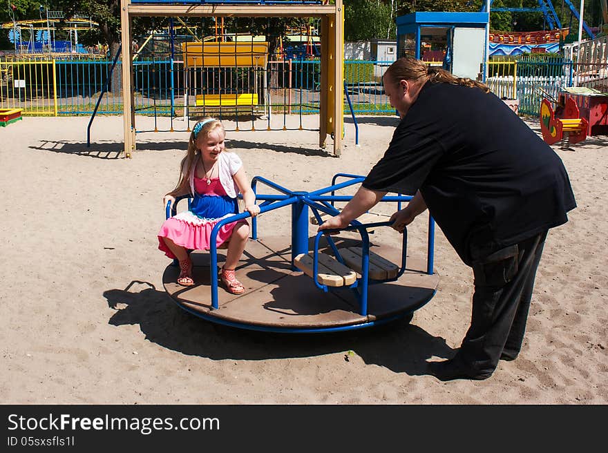 Dad rolls his daughter on a small carousel in the park