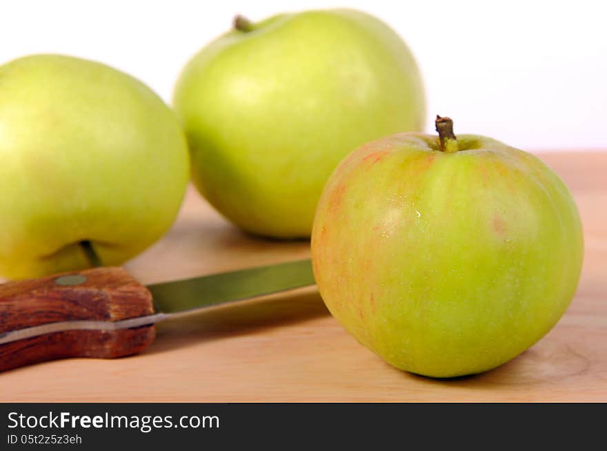 Several green apples and knife on a wooden board