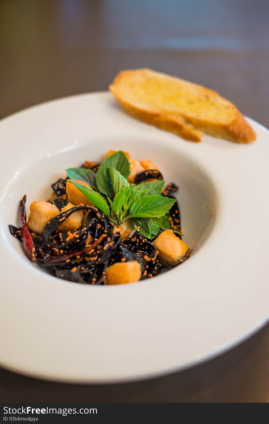 Cooked black pasta noodle served with bread