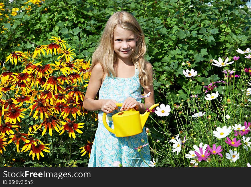 Little girl with watering can near flowers