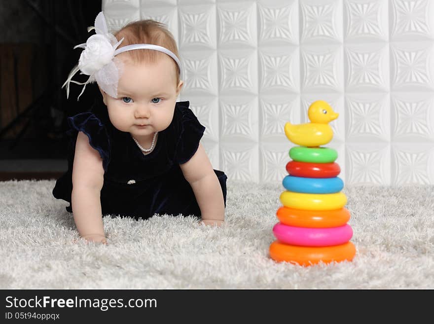 Little cute baby in dress creeps on grey soft carpet among toys. Little cute baby in dress creeps on grey soft carpet among toys.