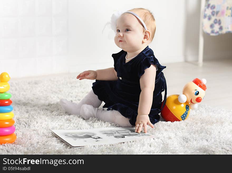 Little cute baby in dress sits on soft carpet among toys and looks up. Little cute baby in dress sits on soft carpet among toys and looks up.