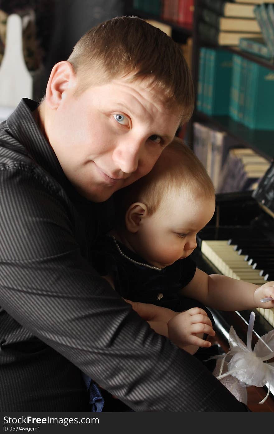 Cute Baby Sits At Knees Of Her Father And Touches Piano