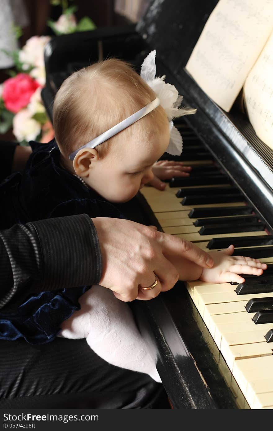 Cute baby sits at knees of father and plays piano