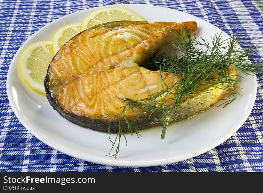 Fried salmon on a plate with lemon and dill on a blue checkered table cloth