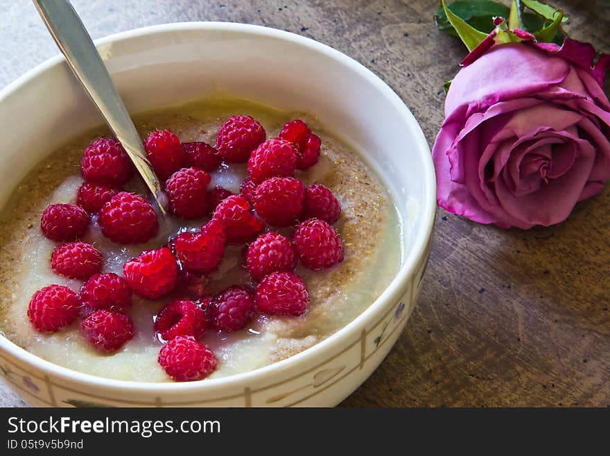 Bowl of porridge with applesauce and fresh raspberries and a rose on the table beside the bowl. Bowl of porridge with applesauce and fresh raspberries and a rose on the table beside the bowl.