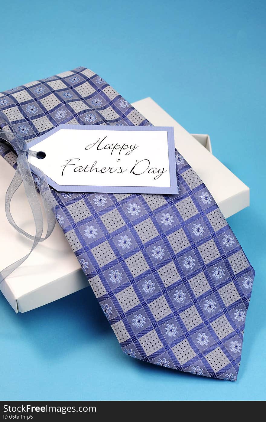 Happy Fathers Day gift of a blue pattern check tie in a white gift box present with gift tag against a blue background. Vertical. Happy Fathers Day gift of a blue pattern check tie in a white gift box present with gift tag against a blue background. Vertical.