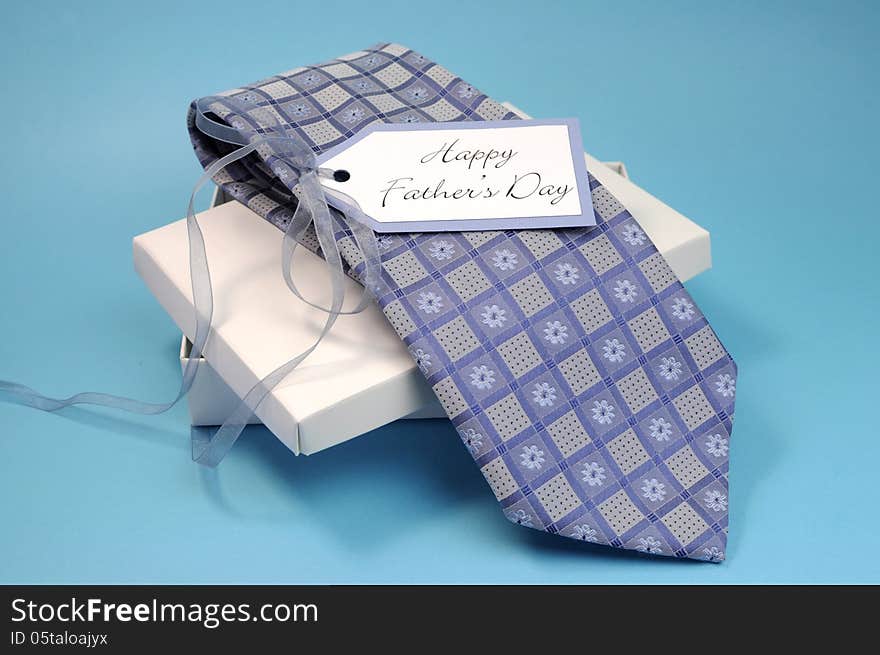 Happy Fathers Day gift of a blue pattern check tie in a white gift box present with gift tag against a blue background.