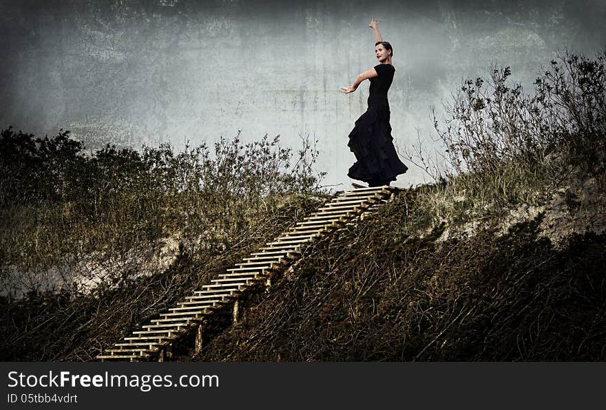 Enigmatic woman in black dancing in the dunes, on the top of the stairs