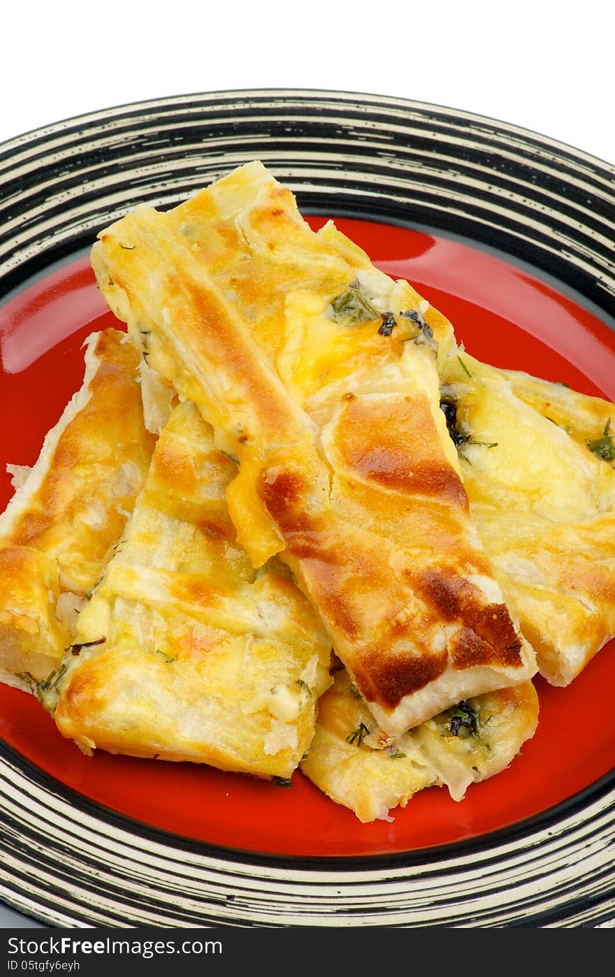 Pile of Cheese and Greens Puff Pastry Pie on Red Striped Plate closeup on white background. Pile of Cheese and Greens Puff Pastry Pie on Red Striped Plate closeup on white background