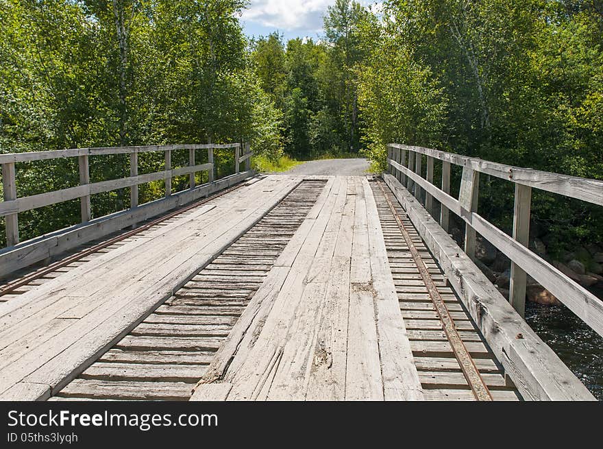 Old wood plank bridge crossing a stream on a gravel logging road in remote Maine woods.