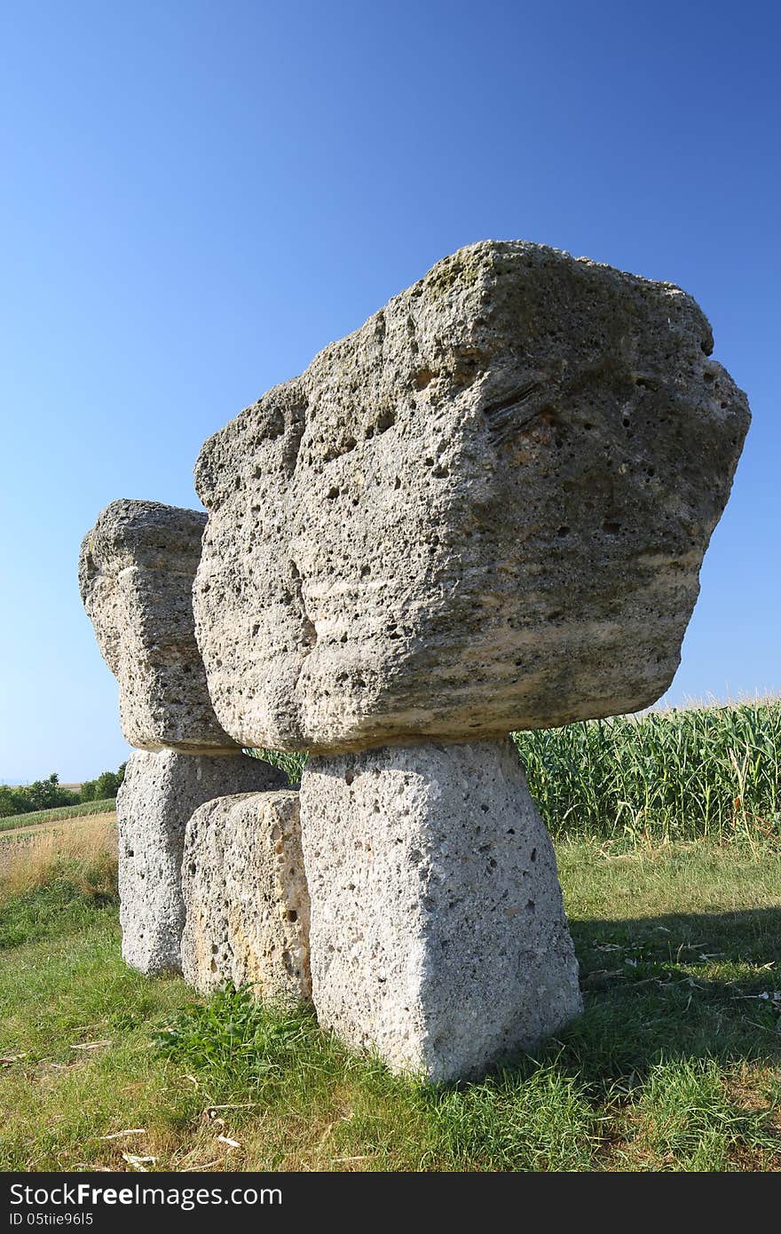 An abstract sulpture consisting of big hewn stone blocks one over the other. The work of art is placed outdoor in the fields in front of a cloudless blue sky. An abstract sulpture consisting of big hewn stone blocks one over the other. The work of art is placed outdoor in the fields in front of a cloudless blue sky