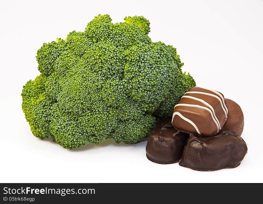 Raw green broccoli and four chocolate candies against a white background. Raw green broccoli and four chocolate candies against a white background