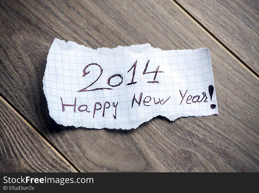 Happy new Year 2014 - Hand writing text on a piece of paper on wood background