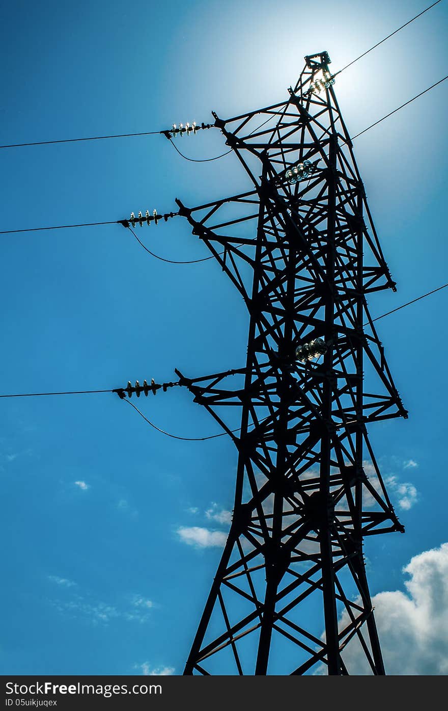 Power pylon and lines against the sun with small amount of clouds on sky. Power pylon and lines against the sun with small amount of clouds on sky