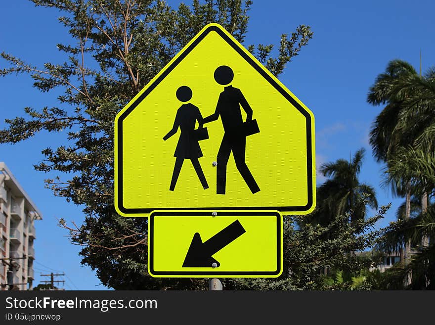 Pedestrian crossing sign in front of blue sky and trees