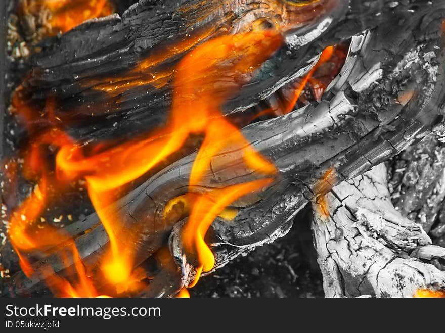 A view into the middle of a wood fire with flames, glowing embers and blackened wood logs with white ashes.