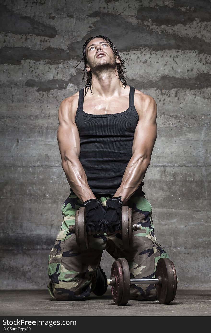 Portrait of handsome athlete lifting weights on wall background