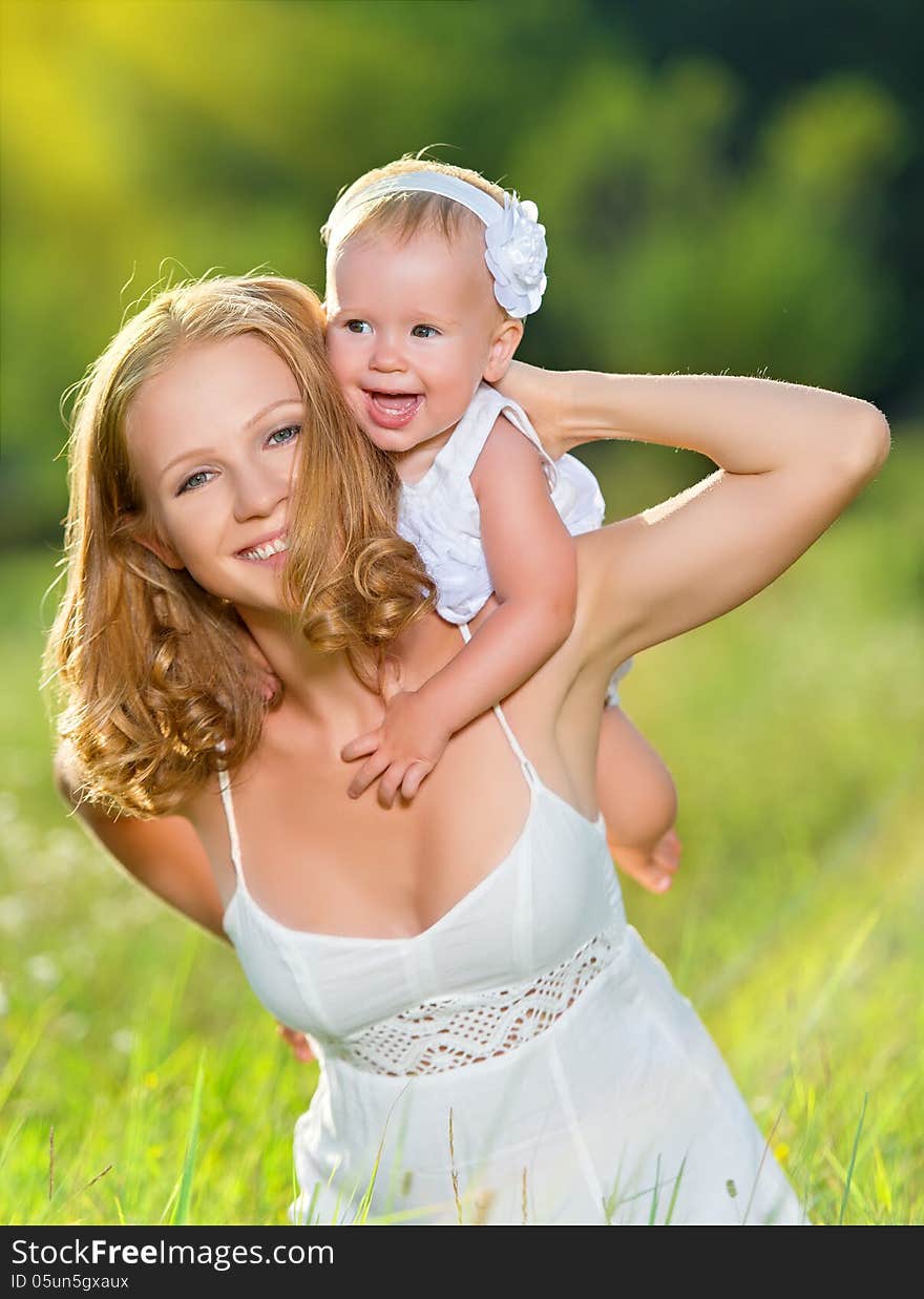 Happy family on nature outdoors mother and baby daughter on the green meadow in a white dress. Happy family on nature outdoors mother and baby daughter on the green meadow in a white dress