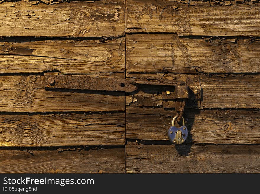 Old rusty padlock on wooden door lit by setting sun distressed texture. Old rusty padlock on wooden door lit by setting sun distressed texture