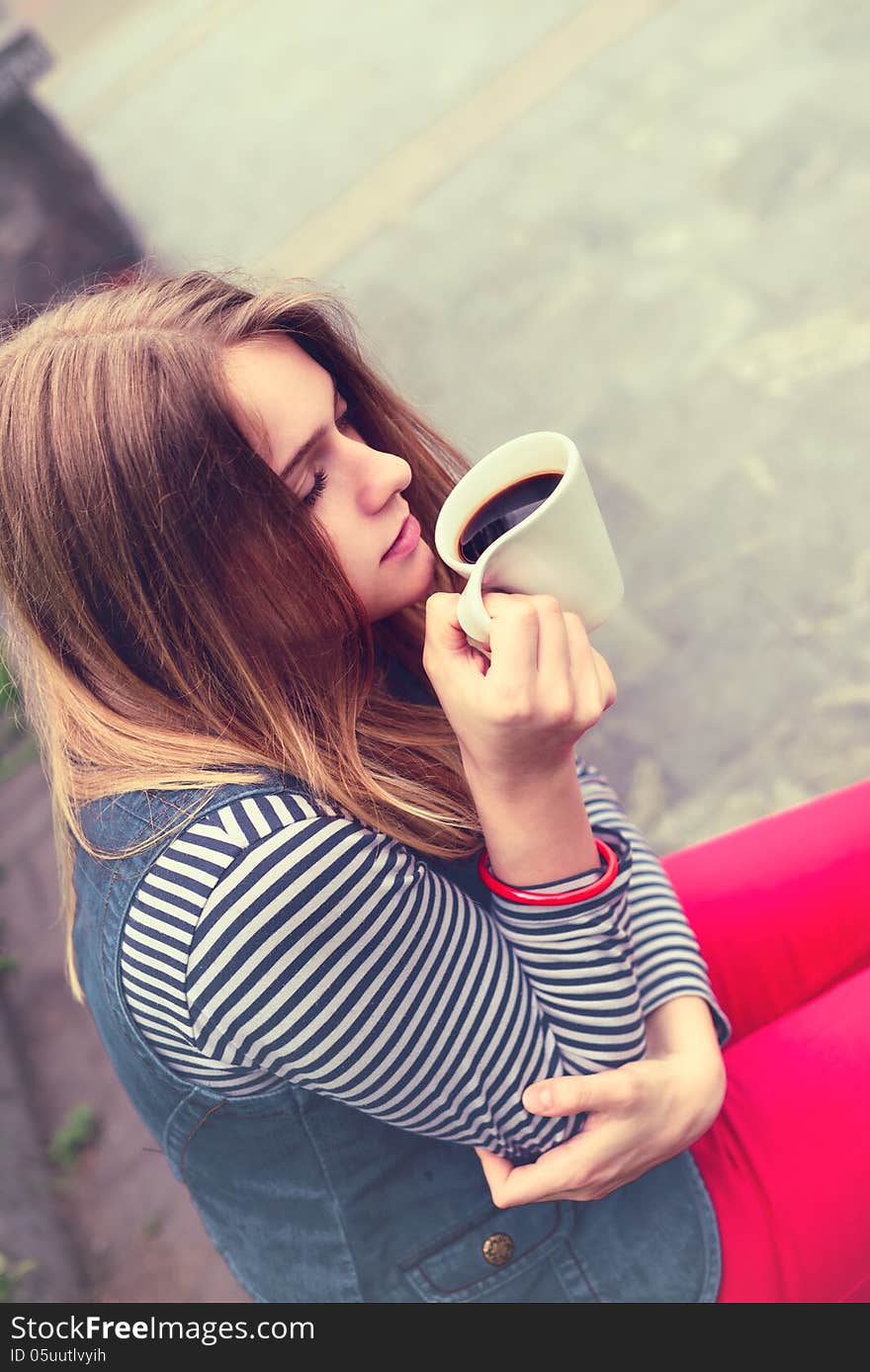 Beautiful girl during a rain under umbrella drinks hot coffee