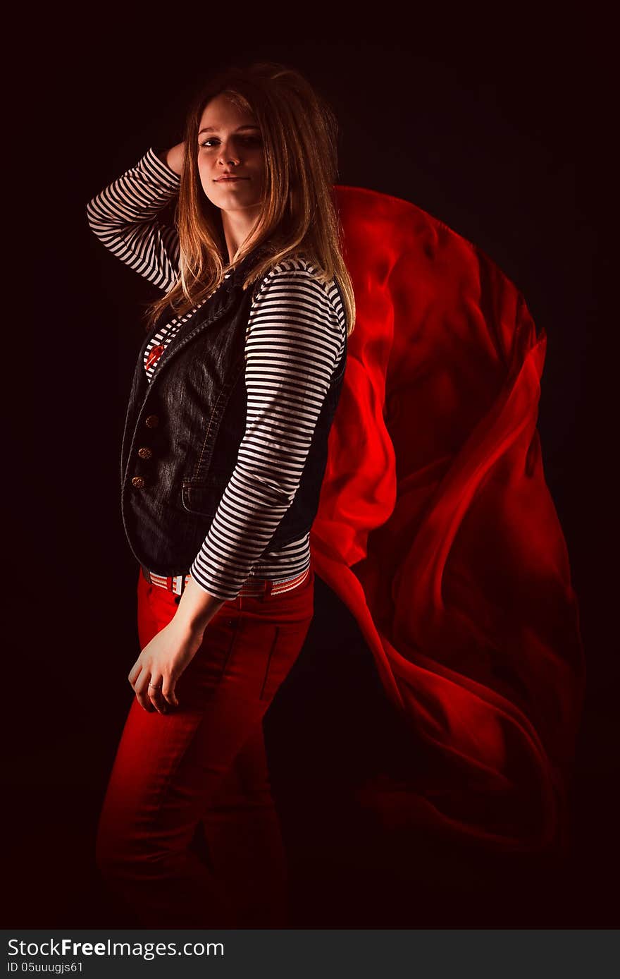 Beautiful girl against red fabric in the dark with long blond hair