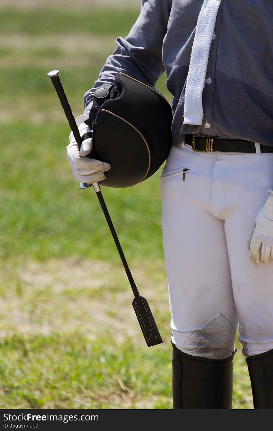 Jockey in uniform with a whip and helment .